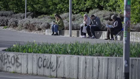 people dressed warmly, sitting on the street, reading and talking
