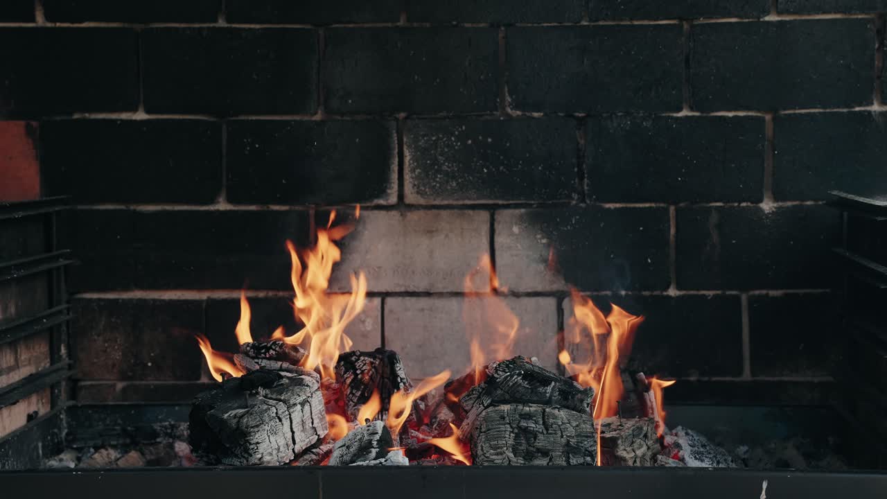 Close up flames rise from wood fire inside dark brick grill glowing with heat