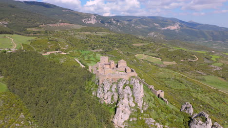 forward drone shot approaching a medieval stone castle on a rocky hill, surrounded by forest, farmland, and rolling hills under a bright sky. scenic rural and historic location in northern spain