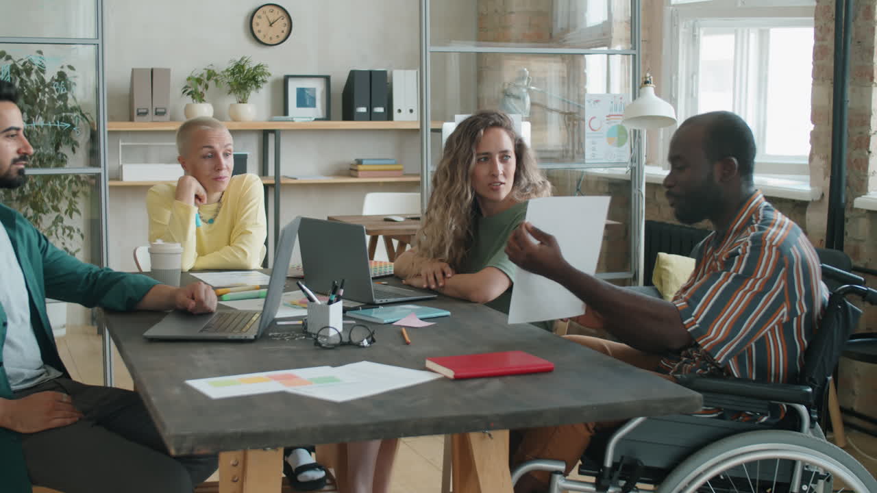 African American Man in Wheelchair Discussing Business Plan with Colleagues at Meeting