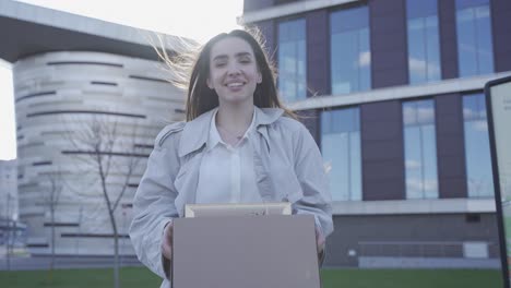 a pretty woman has just quitted her job. she is in front of an office building. she is happy. she is smiling.