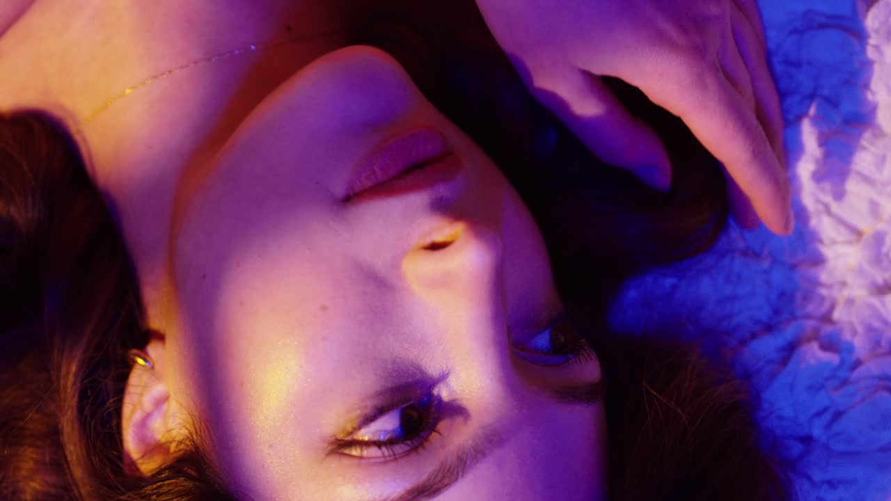 Cinematic top-down close-up of a beautiful woman lying on a bed, featuring a small heart tattoo on her hand, creating an intimate and dreamy mood