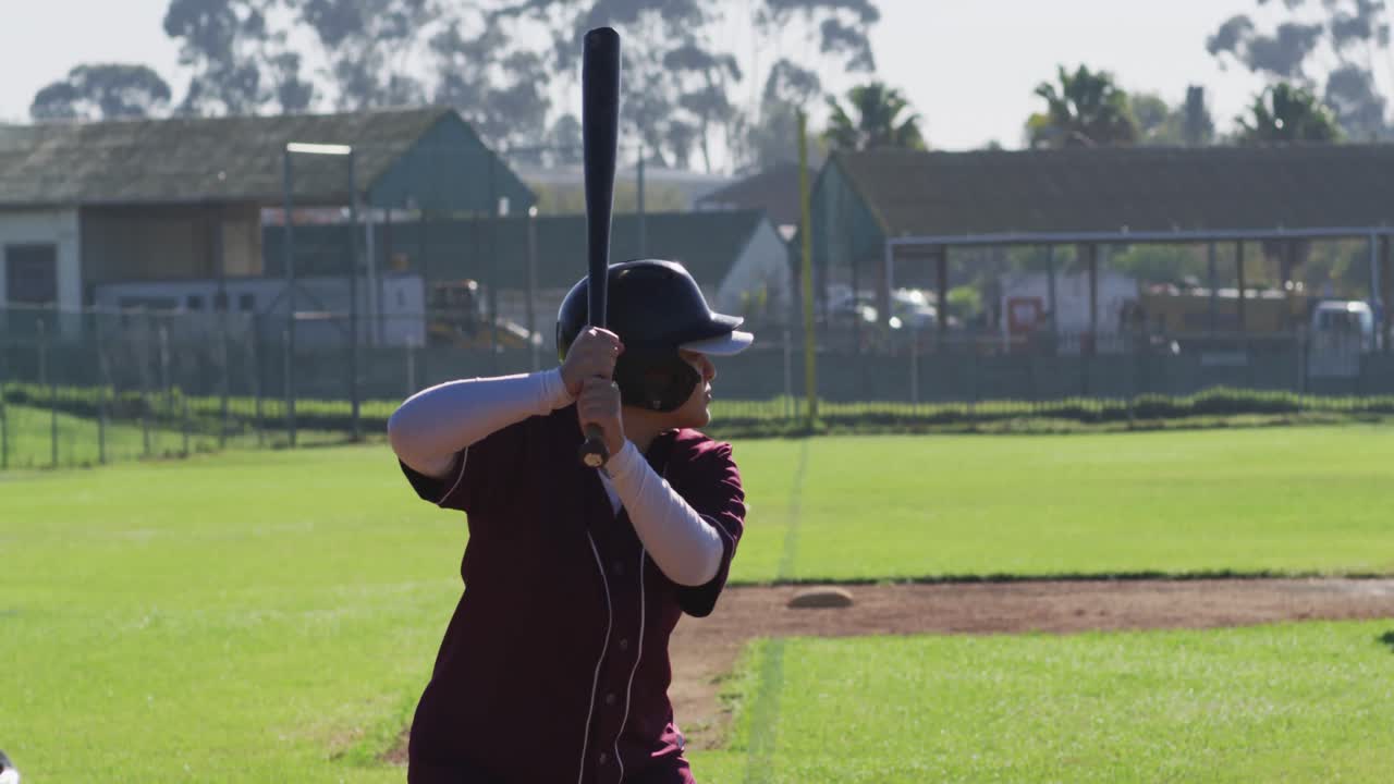 Giocatrice di baseball di etnia mista, battitrice, che sferra la mazza per la palla lanciata.