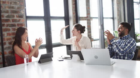 three business professionals celebrate with a high-five in a modern office setting