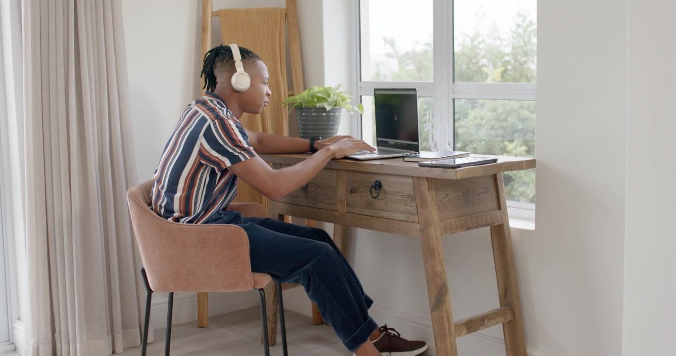 Adult African American man striped shirt headset starting leaning forward typing on laptop at desk