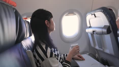 woman sitting inside airplane and looking at window and drinks coffee.