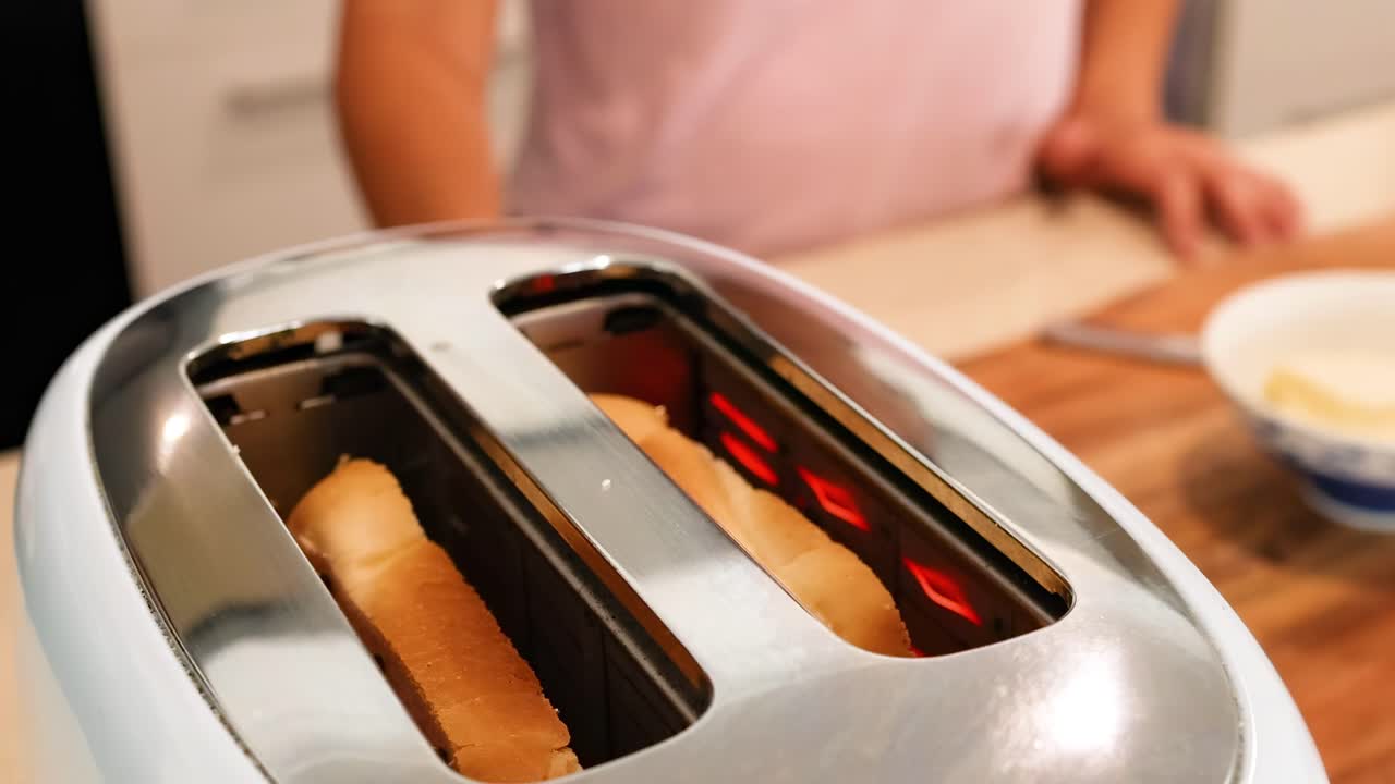 Close-up of a toaster browning bread slices with a person standing nearby in a kitchen setting.
