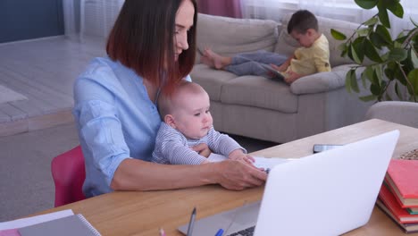 mother looking at her children while working on laptop