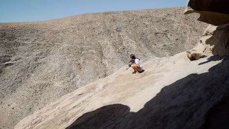 Young-black-latin-woman-play-with-wild-big-bird-on-the-crest-top-of-rock-desert-mountain-in-Fuerteventura-island-canary-Spain-under-hot-sun