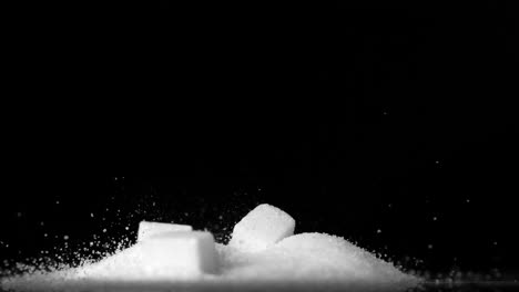 sugar cubes falling into pile of sugar on black background