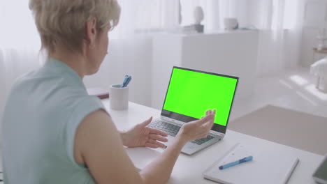blonde-woman-is-communicating-online-by-video-call-looking-at-green-screen-of-laptop-for-chroma-key-technology-gesticulating-and-nodding
