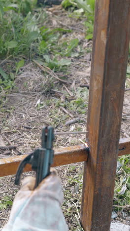 backside view welder in mask connects bottom plank to rusty fence with powerful tool on spring day