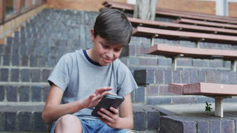 using smartphone, boy sitting on steps outside school, concentrating on screen