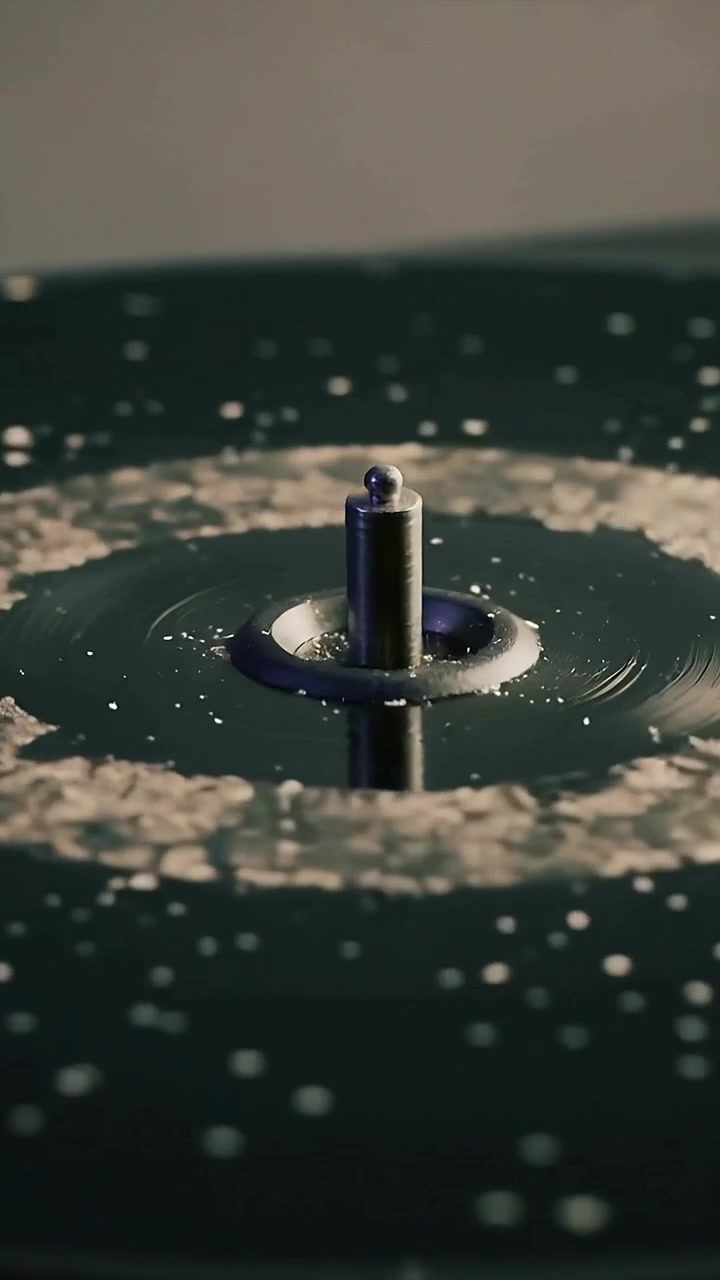 Vertical video: Rotating dish moving pale foam ring around metal post on dark pool, for observation