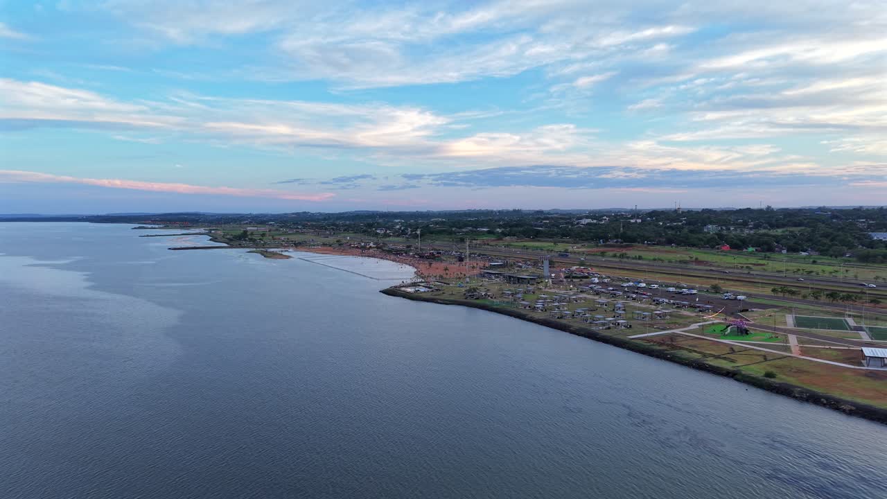 Seguimiento con drones a gran altitud sobre el río Paraná, cerca del balneario Costa Sur. La toma cinematográfica muestra un río tranquilo, nubes en movimiento y tráfico en la carretera costera en Posadas, Argentina.