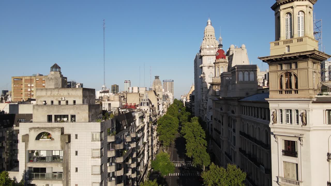 muñeca aérea volando sobre la avenida de mayo rodeada de árboles con la torre del palacio barolo y edificios de buenos aires al atardecer