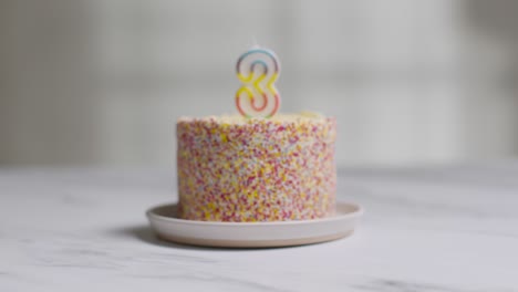 studio shot birthday cake covered with decorations and candle celebrating third birthday being lit