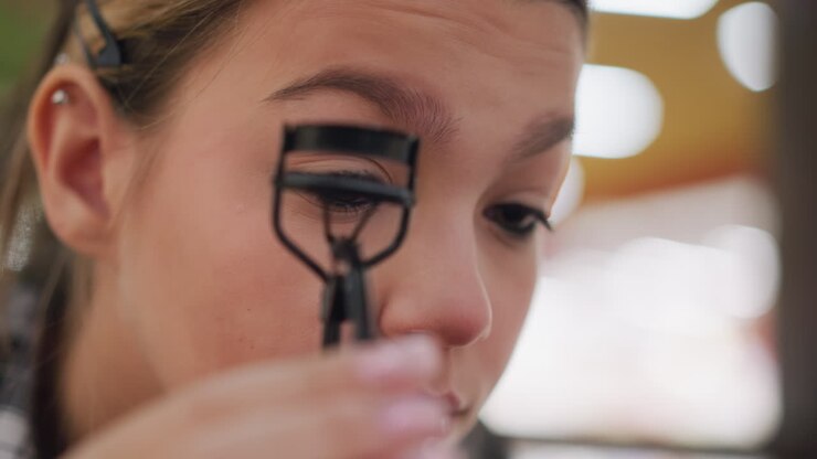 Close-up view of young lady carefully arranging eyelid with eye opener to enhance eye makeup, demonstrating precise beauty techniques for flawless makeup application