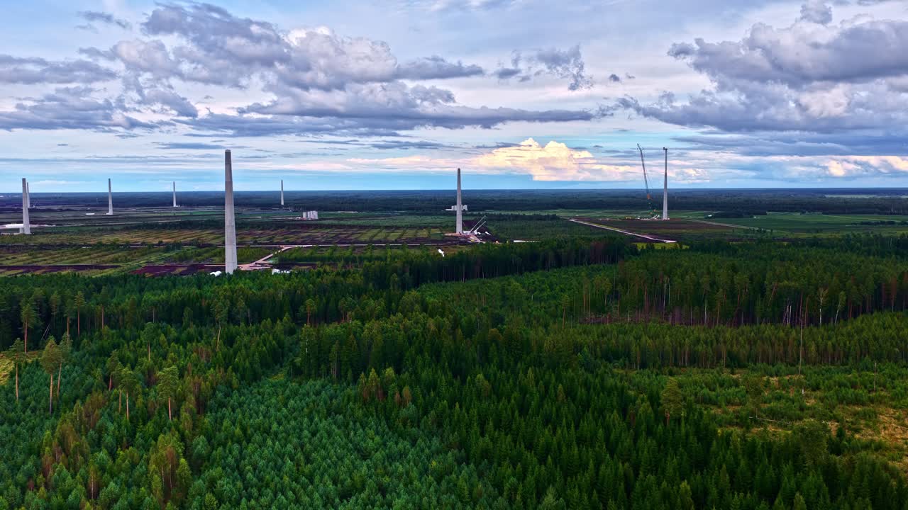 Aerial of wind farm under construction, surrounded by dense green forest under a cloudy sky