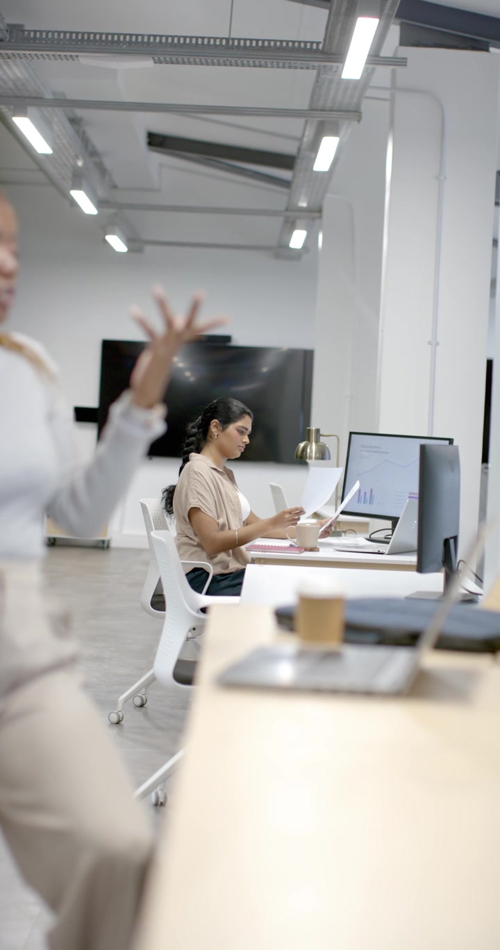 Video verticale: donne diverse in ufficio, una collega che entra parlando al telefono, donna indiana che esamina i grafici.