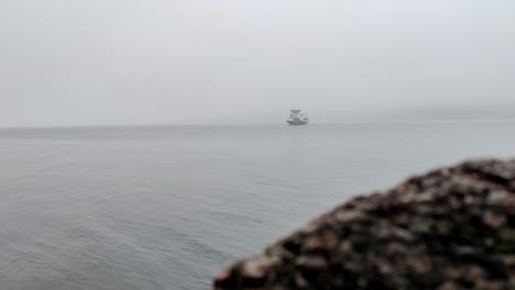 norwegian ferryboat hjellestad crossing fogg fjord leroyosen in reduced visibility outside bergen norway - cinematic clip with blurred sea rock in foreground