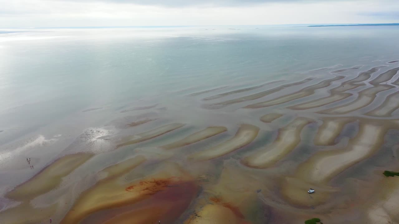 Nantucket coastline at low tide displays exposed sand ridges, tidal flats dotted with reflective tide pools, and dune grass adding texture along the edges of the sandy beach