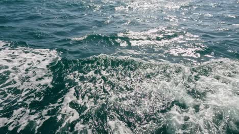 dynamic ocean waves and sunlight reflections captured behind a moving fishing boat near rawai beach, phuket, thailand