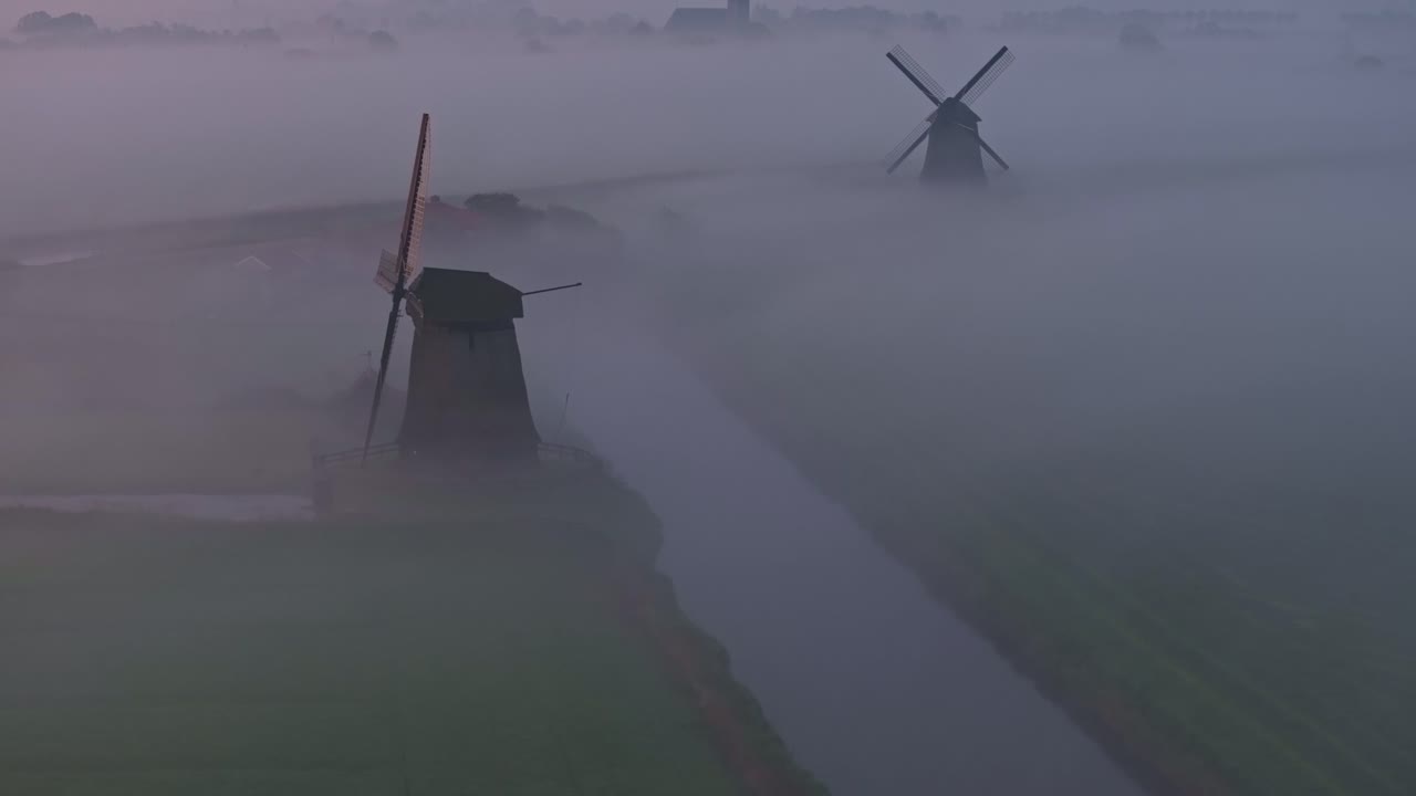 Windmolens en de Grote Kerk in het mistige Schermerhorn, Nederland