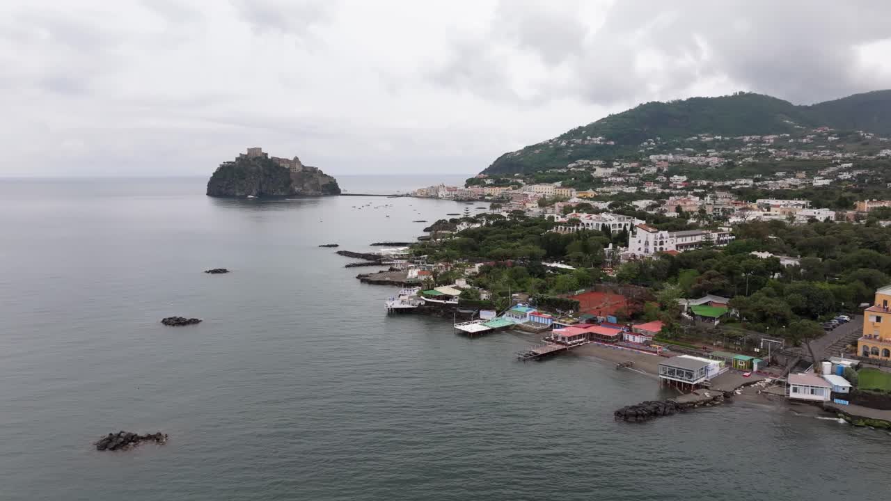 Orbita di drone intorno a case sulla spiaggia sull'isola d'Ischia, con il famoso castello roccioso sullo sfondo.