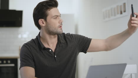 Cheerful-man-holding-smartphone-for-picture-at-living-room.