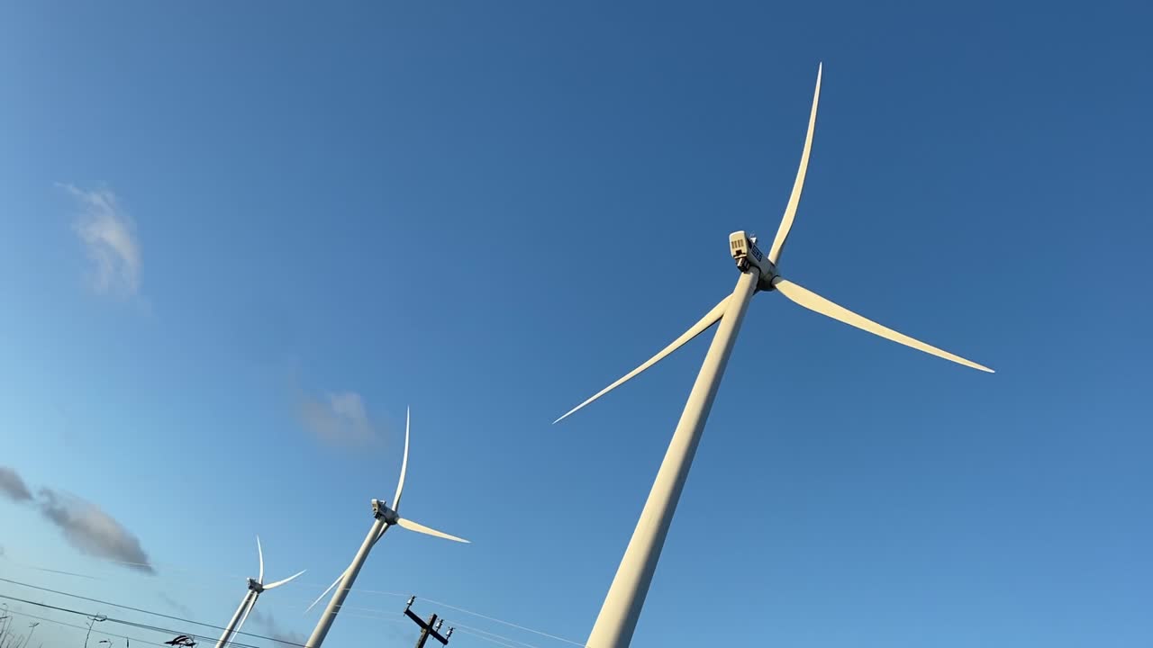 푸른  ⁇ 빛 하늘 아래 풍력 터빈이 일치하여 회전합니다.