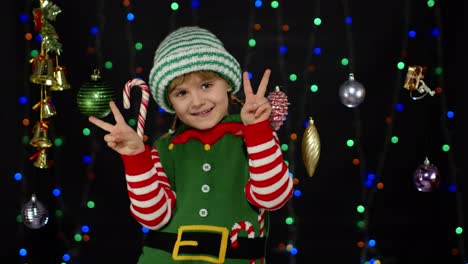 niña rubia en el elf de navidad disfraz de ayudante de santa claus haciendo un gesto de paz, mostrando el signo v