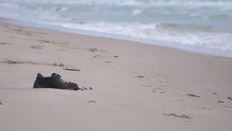 Black-shoe-on-the-beach,-trash-and-waste-litter-on-an-empty-Baltic-sea-white-sand-beach,-environmental-pollution-problem,-overcast-day,-medium-shot