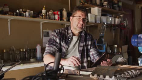 caucasian male knife maker in workshop, using tablet and smiling