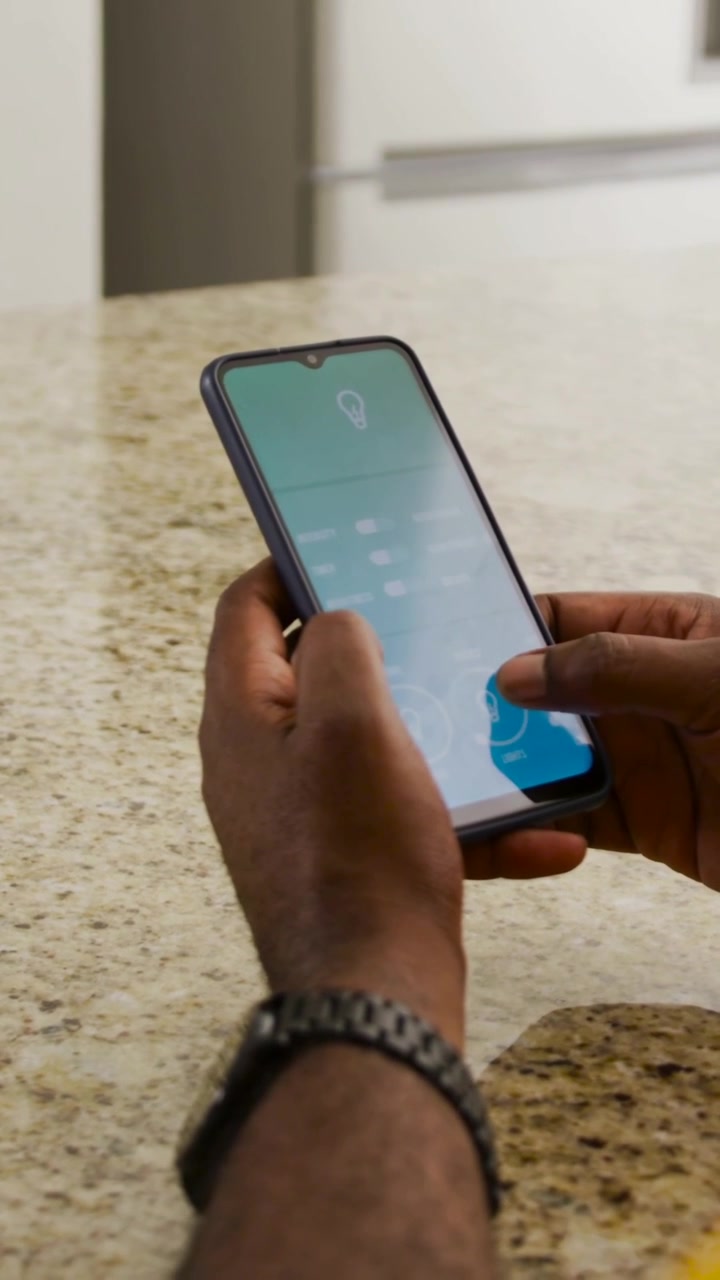 Tapping yellow-shirt man adjusting phone bulb app on speckled counter in kitchen, confirming