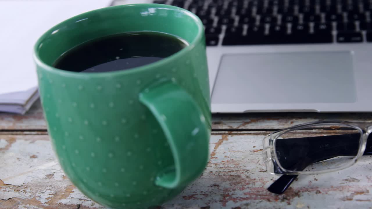 Green coffee mug staying still, faint HUD icons appearing and aligning above laptop showing tools