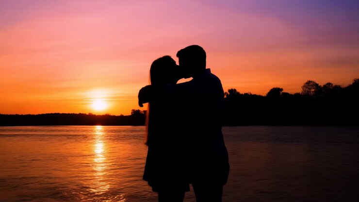 Casal em Silhueta se Beijando ao Pôr do Sol à Beira do Lago, Céu Quente Laranja e Roxo, Reflexo na Água, Abraço Suave
