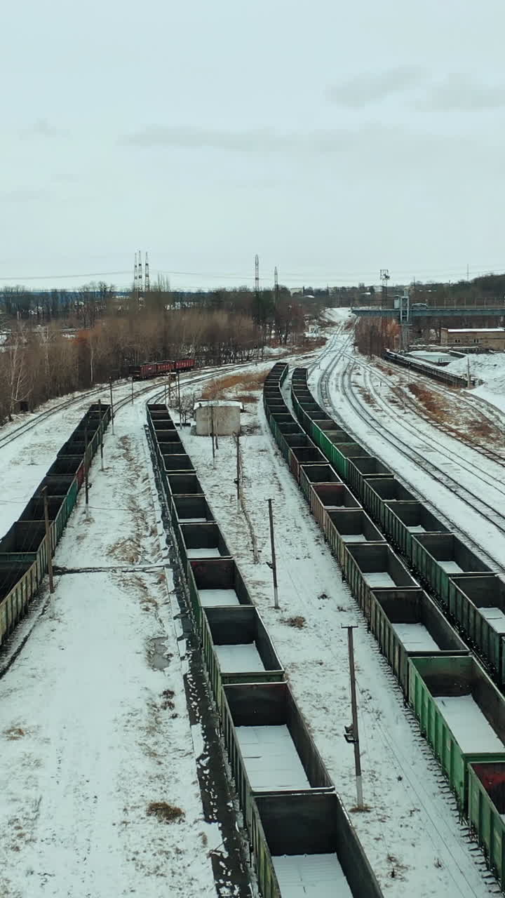 Long rows of containers stand on rails on the territory of the railway. Shipping. Camera motion to back. Aerial view. Vertical video