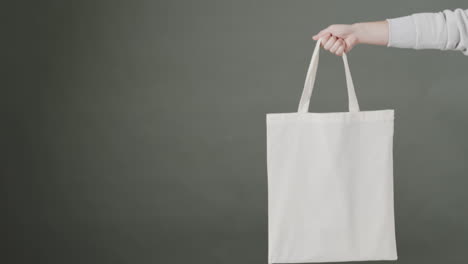 la mano de una mujer caucásica sosteniendo una bolsa blanca sobre un fondo gris, copia el espacio, cámara lenta.
