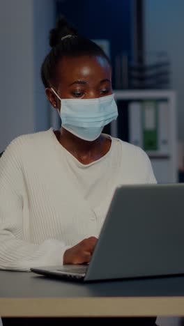 vertical video african woman with face mask reading emails late at night to respect deadline