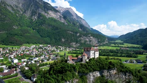 Luftaufnahme-Des-Weißen-Schlosses-Mit-Rotem-Dach-In-Liechtenstein-Mit-Stadt-Unten-Und-Bergen