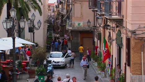 pedestrians walk pass lamps and brick buildings within close proximity of one another in cefalu italy