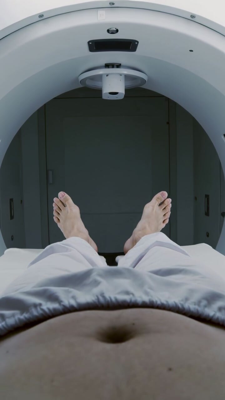 Vertical video: Sliding table carrying patient into gantry in clinic gown over pelvis coil aligning