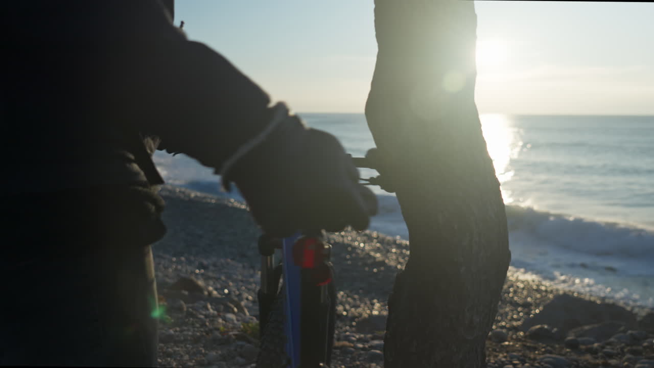 남자는 나무에 기대어 있는 산악 자전거를 타고 아침 햇살에 흠뻑 젖은 멋진 해안 풍경을 남기고 출발합니다.