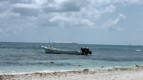 view from the beach of an empty boat floating in the ocean