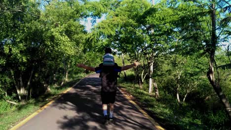 padre e hijo caminando en un parque público, el hijo está sentado en el cuello de su padre mientras camina