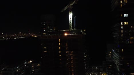 Construction-site-and-crane-welder-working-on-building-at-night,-aerial-overview