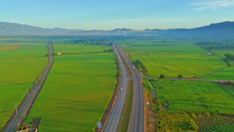 aerial view of highway cutting through lush green rice paddies and mountains
