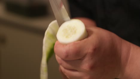 un chef sosteniendo en una mano el pepino y cortándolo alrededor de la circunferencia haciendo una hoja de pepino para el rollo de sushi.