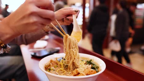 person eating noodles with chopsticks in busy restaurant